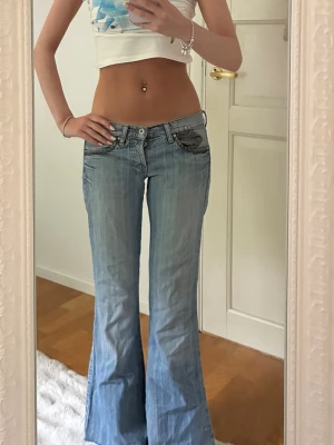 Ljusblå bootcut jeans från Americanos - Säljer ett par ljusblå bootcut jeans från Americanos med låg midja och klassiska kontrastsömmar. Jeansen har fickor fram och bak samt detaljerade sömmar på bakfickorna. Perfekta för en trendig och avslappnad look. Storleksklassen är utsuddad men uppskattar xs/s. 