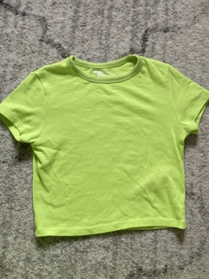 Limegrön croppad topp från FB Sister - Snygg limegrön croppad topp från FB Sister i slim fit-modell. T-shirten har korta ärmar och rund halsringning, perfekt för dig som gillar färg och enkel stil. Tillverkad i mjuk bomull som känns skön mot huden.