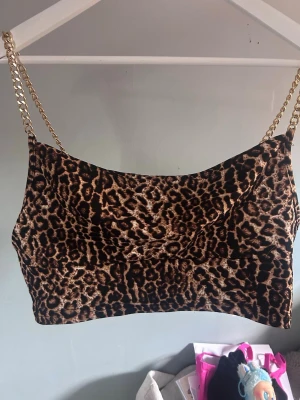 Leopardmönstrad croppad linnetopp - Snygg croppad linnetopp med leopardmönster och guldfärgade kedjeaxelband. Perfekt för dig som vill sticka ut och addera lite edge till din outfit. Tunn och mjuk känsla, passar till både jeans och kjol.