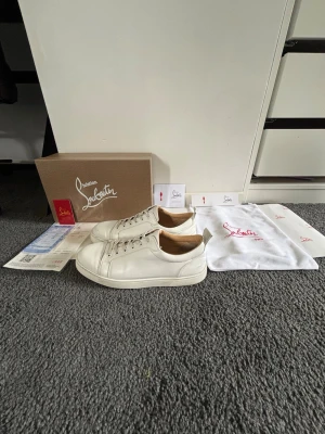 Vita Christian Louboutin sneakers - Snygga vita sneakers från Christian Louboutin i läder med klassisk röd sula och diskret logga på sidan. Skorna har lågt skaft, vita snören och en clean design som passar till det mesta. Kommer med originalkartong, dustbags och certifikat.
