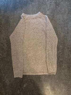 Beige stickad tröja med rund hals - En enkel och stilren beige stickad tröja med rund hals och långa ärmar. Tröjan har en klassisk rak passform och ribbstickade muddar vid hals, ärmslut och nederkant. Perfekt basplagg för lager på lager och passar till det mesta.