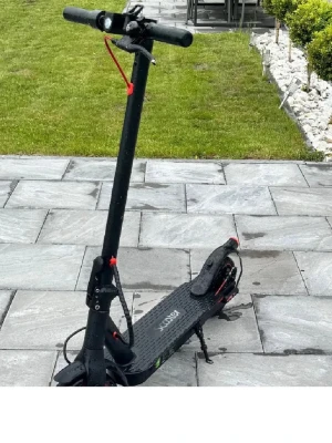 Svart elscooter  - Säljer en svart elscooter med röda detaljer. Scootern har bred fotplatta med halkskydd, stora hjul och handtag med bra grepp. Perfekt för smidig transport i stan eller till skolan. Laddas enkelt via eluttag och har stödben.