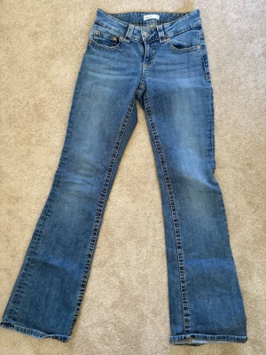 Blå bootcut jeans från H&M - Snygga blå bootcut jeans från Gina tricot med klassisk design och slitna detaljer. Jeansen har normal midja, dragkedja och knapp framtill samt kontrastsömmar. Perfekta för en avslappnad och trendig look.