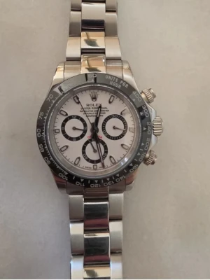 Panda Daytona - Säljer en stilren Daytona med silverfärgat armband i metall och svartvit urtavla. Klockan har tre mindre urtavlor, svart bezel med tachymeterskala och klassisk länkdesign. Perfekt för dig som gillar exklusiva klockor och tidlös design. Sveper vackert med automatisk mekanism, alltså inget batteri i. Länkar följer med, då jag har kortat ner. Säljes bara för att jag ska köpa en Daytona med grön urtavla.