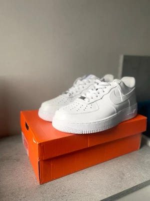 Nike Air Force 1 vita sneakers - Klassiska helvita Nike Air Force 1 sneakers i lågt utförande. Skorna har en stilren design med perforerad tå, vit sula och ikoniska Swoosh-loggan på sidan. Tillverkade i läder med snörning och bekväm passform. Perfekta för dig som gillar en clean och tidlös look.
