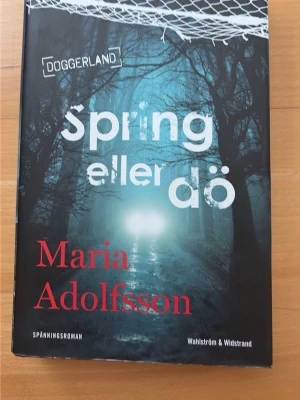 Spring eller dö av Maria Adolfsson - Spännande roman från Doggerland-serien av Maria Adolfsson. Omslaget är mörkt med blå och svarta toner, skogsmotiv och vit samt röd text. Inbunden bok med dramatisk och mystisk känsla, perfekt för dig som gillar deckare och thrillers.