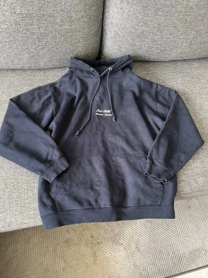 Mörkgrå hoodie Zero Cold - Snygg mörkgrå hoodie från Zero Cold med broderad text på bröstet. Klassisk känguruficka framtill och justerbar huva med dragsko. Perfekt för chill dagar eller när du vill ha en enkel men stilren look.