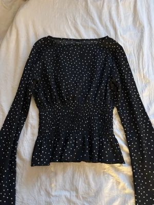 Svart prickig långärmad topp från Gina  - Snygg svart topp med vita prickar och långa ärmar. Toppen har smock i midjan som ger en figurnära passform och lätt volang nedtill. Toppen är från Gina Tricot och endast använd fåtal gånger. Kan ge fler bilder om de önskas!💛