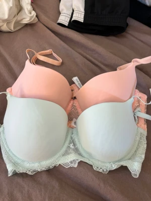 2-pack bhar med spets från Primark - Säljer ett 2-pack bhar från Primark i storlek 75B. En bh är ljusrosa och den andra är ljusblå, båda med vadderade kupor och fina spetsdetaljer nedtill. Justerbara axelband och mjukt material för extra komfort. Perfekta för dig som gillar söta och stilrena underkläder.