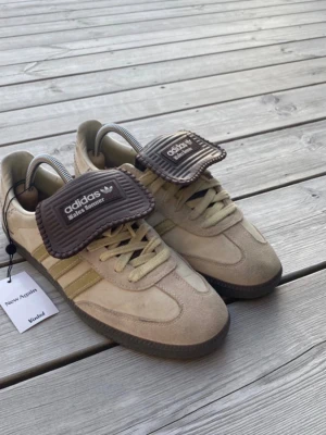 Adidas Wales Bonner beige sneakers - Unika Adidas Wales Bonner sneakers i beige mocka och läder med bruna detaljer och breda tunga i ribbat tyg. Klassiska tre ränder i ljusgul på sidan och mörkbrun yttersula. Snygg retrostil och cool design som sticker ut.