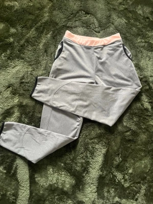 Grå leggings med rosa midja - Snygga grå leggings med bred rosa midjeresår och svarta detaljer vid benslut och sidor. Perfekta för träning eller chill, med en bekväm passform och stretchigt material som följer kroppen. Stilren design som funkar till många outfits.💕💕💕