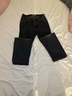 Svarta bootcut jeans med låg midja - Säljer ett par svarta bootcut jeans med låg midja. Jeansen har utsvängda ben och är tillverkade i ett mjukt denimtyg.