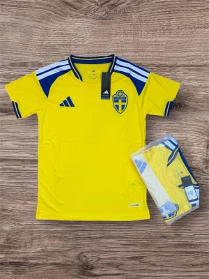 Svensk fotbollströja Adidas gul/blå - Gul fotbollströja från Adidas med blå detaljer och Sveriges landslagsemblem på bröstet. Tröjan har korta ärmar, blå/vita ränder på axlarna och är tillverkad i ett lätt, ventilerande funktionsmaterial. Perfekt för match eller träning.