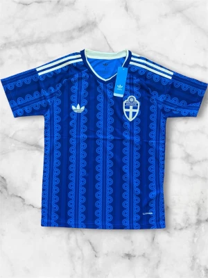 Blå Sverige fotbollströja Adidas - Säljer en blå fotbollströja från Adidas med Sveriges landslagsemblem på bröstet. Tröjan har ett unikt mönster i olika blå nyanser, vita Adidas-ränder på axlarna och rund halsringning med ljusblå kant. Perfekt för match eller träning.