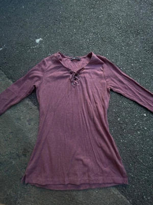 Långärmad ribbad topp med snörning - Långärmad topp från F8 Sister i en dammig rosa nyans. Toppen är ribbad och har snygg snörning framtill vid halsen. Perfekt till jeans eller kjol för en trendig look.