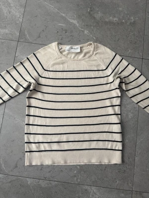 Randig stickad tröja från Selected Femme - Snygg stickad tröja från Selected Femme i krämvitt med tunna svarta horisontella ränder. Tröjan har rund halsringning och långa ärmar. Perfekt för en stilren och avslappnad look.
