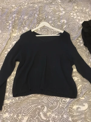 Mörkblå stickad tröja med V-ringning - En enkel och stilren mörkblå stickad tröja med V-ringad hals. Tröjan har långa ärmar och ribbade muddar vid ärmslut och nederkant. Perfekt att matcha med jeans eller kjol för en avslappnad look.