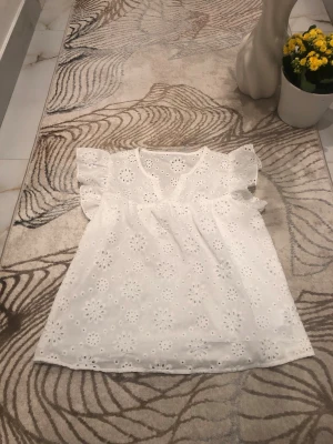 Vit blus med volangärmar och broderi - Söt vit blus med broderade blommor och volangärmar. Blusen är ärmlös med rund halsringning och har ett luftigt, lätt material som passar perfekt till sommaren. Den har en romantisk och fräsch look som är enkel att styla. Använd endast ett fåtal gånger. Är öppen för prisförslag😊