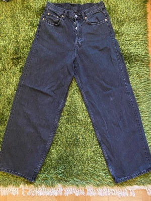 Weekday Svarta Astro Loose Baggy Jeans - Säljer ett par svarta Astro Loose Baggy jeans från weekday. Klassisk femficksmodell med silverfärgade nitar och knappstängning. Jeansen har en avslappnad passform och är tillverkade i kraftigt denim.