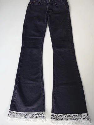 Svarta utsvängda jeans med spets - Svarta jeans med utsvängda ben och vit spetsdetalj längst ner vid bensluten. Ett par från början vanliga Gina byxor men nu med unika detaljer.