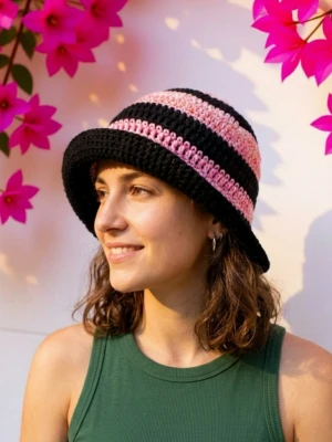 Randig virkad bucket hat svart rosa - Säljer en handvirkad bucket hat med breda ränder i svart och ljusrosa. Hatten har en klassisk form med nedåtlutande brätte och är tillverkad i ett mjukt garnmaterial. Perfekt för att addera färg till din outfit.