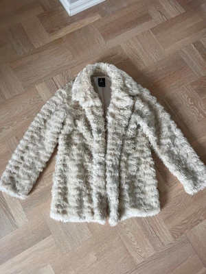 Beige fuskpälsjacka från Atmosphere - Säljer en fluffig och trendig vit fuskpälsjacka från Atmosphere. Jackan har en mjuk struktur och knappar framtill. Perfekt för dig som vill ha en statementjacka och gillar en lyxig look. En av fickorna har en trasig söm på insidan, inget som syns. 