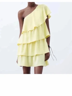 Gul one shoulder volangklänning från zara - Helt ny med lapp!! Säljer en ljusgul kortklänning med flera volanglager och oneshoulder-design. Klänningen har en luftig och somrig känsla, perfekt för varma dagar. Materialet känns lätt och svalt, och modellen har en lös passform med snyggt fall.