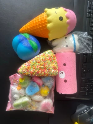 Squishy paket - Ett paket med flera squishies i olika former och färger, bland annat en glass, en blå bulle, en tårtbit med strössel, en rosa cylinder med björnansikte och en påse med små squishies i olika pastellfärger. Perfekt för dig som gillar kawaii och stressleksaker.