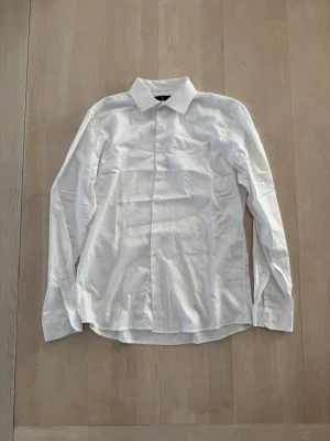Klassisk vit skjorta med knappar - Stilren vit skjorta med klassisk krage och knäppning framtill. Skjortan har lång ärm och är tillverkad i ett mjukt bomullstyg som passar perfekt till många olika looks. Enkel och tidlös design som är lätt att matcha.