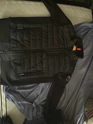 Svart quiltad jacka från Parajumpers - Snygg svart quiltad jacka från Parajumpers med dragkedja framtill och tre dragkedjeförsedda fickor. Jackan har lång ärm och en liten patch på ena ärmen. Perfekt för dig som vill ha en stilren och sportig look.