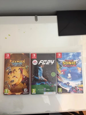 Nintendo Switch spel Rayman, FC24, Sonic - Säljer tre Nintendo Switch spel: Rayman Legends med färgstark fantasyvärld, FC24 med sporttema och fotboll, samt Team Sonic Racing med blåa och färgglada karaktärer i racingmiljö. Alla spel har plastfodral och tydliga omslag.