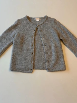 Grå basic kofta med rund hals storlek:134-140 - Mysig grå kofta med rund halsringning och knappar framtill. Tillverkad i mjukt stickat material som känns skönt mot huden. Långärmad modell som passar perfekt till lager på lager och funkar året runt.