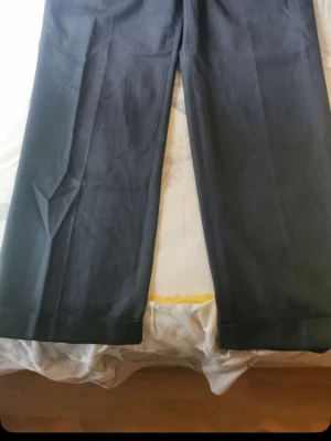Svarta vida kostymbyxor - Säljer ett par svarta kostymbyxor med rak och vid passform. Byxorna har pressveck framtill och är tillverkade i ett slätt tyg som ger en klassisk look. Perfekta för dig som gillar stilrena och tidlösa plagg.