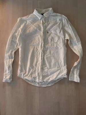Vit skjorta med diskreta ränder - Klassisk vit skjorta med subtila ränder och bröstficka. Skjortan har lång ärm, knappar framtill och en tidlös krage. Perfekt för dig som gillar en clean och stilren look.