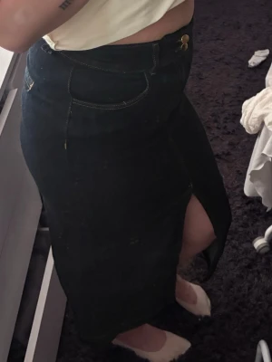 Mörkblå jeanskjol med slits Stockh Lm - Säljer en mörkblå lång jeanskjol från Stockh LM. Kjolen har klassiska jeansdetaljer som fickor, synliga sömmar och knappar framtill. Den har en snygg slits framtill som ger extra edge till looken. Perfekt att styla med sneakers eller boots.