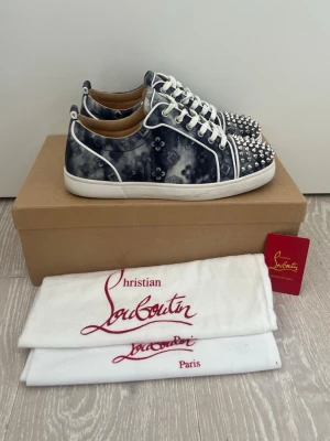 Christian Louboutin blå sneakers - Unika sneakers från Christian Louboutin i blått och vitt med coolt mönster och silverfärgade nitar på tån. Skorna har vita snören, vita detaljer och en klassisk låg siluett. Insidan är i beige läder och yttermaterialet har en tvättad denim-look.Begränsat tillbehör ingår 1 dustbag box skor ingår i priset.