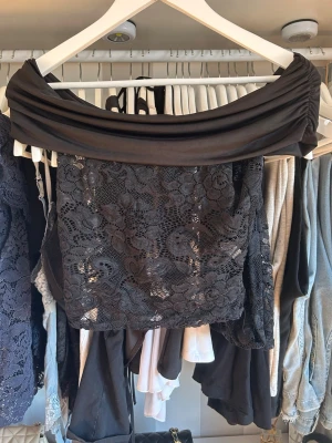 Svart offshoulder spets topp Fashion Nova - Säljer en svart offshoulder topp från Fashion Nova i storlek S. Toppen har ett brett omlottband över axlarna och är tillverkad i spets med blommigt mönster. Perfekt för dig som vill ha en trendig och elegant look.