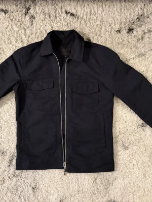 Mörkblå overshirt från Elvine - Snygg mörkblå overshirt från Elvine med raka linjer och två bröstfickor. Jackan har dragkedja framtill och klassisk krage. Perfekt för lager på lager och enkel att matcha med olika outfits.