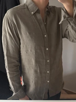 Olivgrön linneskjorta från John Henric  - Stilren olivgrön skjorta i 100% linne med klassisk krage och vita knappar hela vägen framtill. Skjortan har långa ärmar och en avslappnad passform, perfekt för en trendig och bekväm look. Passar till jeans eller chinos för en enkel men snygg outfit. Lite nopprig annars bra skick 