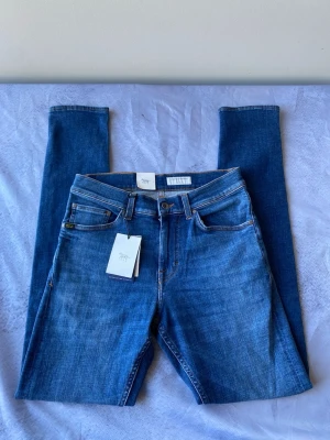 Blå slim jeans från Tiger of Sweden-29/34 - Snygga blå slim jeans från Tiger of Sweden med klassisk femficksmodell och orangea kontrastsömmar. Jeansen har normal midja och är tillverkade i mjuk bomullsdenim. Perfekta för en trendig och avslappnad look.