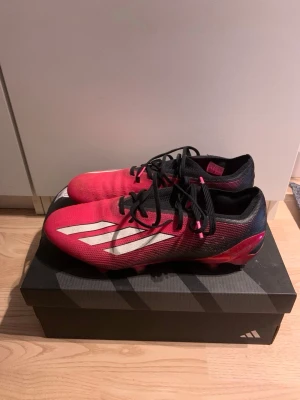 Adidas röda fotbollsskor med skrubdobbar  - Snygga fotbollsskor från Adidas i rött med svarta och vita detaljer. Skorna har klassiska tre vita ränder på sidan, svarta skosnören och skruvdobbar för bra grepp på gräsplaner. Säljer för att dem är för små. Kommer med box, munstycke till skruvdobbar samt med extra skruvdobbar. Pris kan diskuteras.