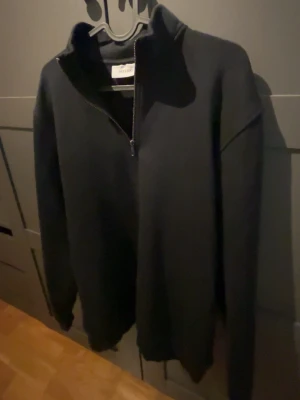 Svart halvzip tröja från Soft Goat - Mörk, stilren halvzip tröja från Soft Goat i svart. Tröjan har hög krage med dragkedja och långa ärmar. Perfekt för dig som gillar en clean och enkel look. Materialet ser ut att vara mjukt och av hög kvalitet.