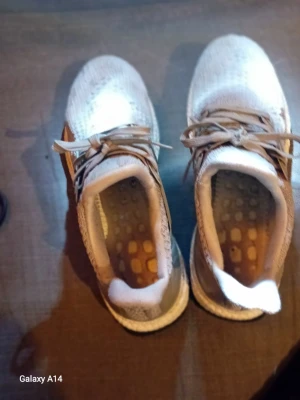 Vita sneakers med stickad ovandel - Snygga vita sneakers med stickad mesh-ovandel och bruna detaljer. Skorna har snörning och en bekväm, dämpad sula med synliga hål i innersulan för extra ventilation. Perfekta för dig som gillar sportig och modern stil.