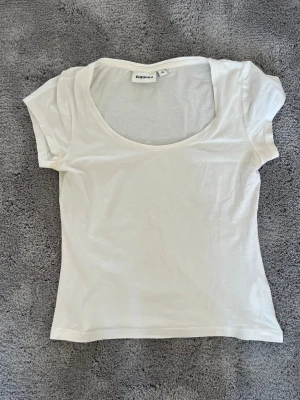 Vit t-shirt med rund hals Kappahl - En basic vit t-shirt från Kappahl med rundad, djup halsringning och korta ärmar. Tillverkad i mjukt och tunt material som känns skönt mot huden. Perfekt att matcha med jeans eller kjol för en clean och enkel look.