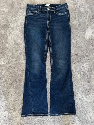Blå bootcut jeans från Gina Tricot - Snygga blå bootcut jeans från Gina Tricot med kontrastsömmar och klassisk femficksmodell. Jeansen har en mörk tvätt och lätt utsvängda ben, perfekta för en trendig och avslappnad look. Materialet är mjukt denim som sitter skönt hela dagen.