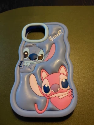 Blått Stitch mobilskal i silikon - Säljer ett blått mobilskal med 3D-design av Stitch och Angel från Disney. Skalet är gjort i mjukt silikon och har vågiga kanter. Passar iPhone 15 XS Max. Perfekt för dig som gillar söta och färgglada motiv!