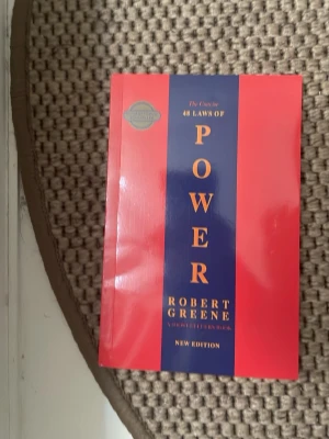 The Concise 48 Laws of Power book - Säljer boken 'The 48 Laws of Power' av Robert Greene. Boken har ett rött och blått omslag med guldfärgad text. Perfekt för dig som gillar psykologi, strategi och maktspel. Pocketutgåva, engelska.