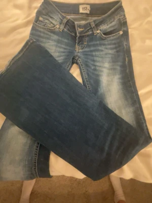 Blå jeans från 157 blaze - Säljer ett par blå jeans från 157 med snyggt slitna detaljer och klassisk femficksmodell. Jeansen har normal midja och raka ben. Materialet är denim med en tvättad look som ger en avslappnad stil. Perfekta för dig som gillar en casual vibe.