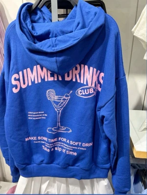 Blå hoodie med rosa tryck Summer Drinks - Cool blå hoodie med stor huva och rosa texten 'SUMMER DRINKS' på ryggen. Trycket har även en drinkillustration och flera mindre texter.  mjukt material, perfekt för chill dagar. 