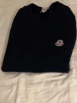 Mörkblå sweatshirt från Moncler - Snygg mörkblå sweatshirt från Moncler med klassisk rund halsringning och Moncler-logga broderad på bröstet. Perfekt för dig som gillar stilrena och exklusiva plagg. Materialet känns mjukt och bekvämt mot huden.